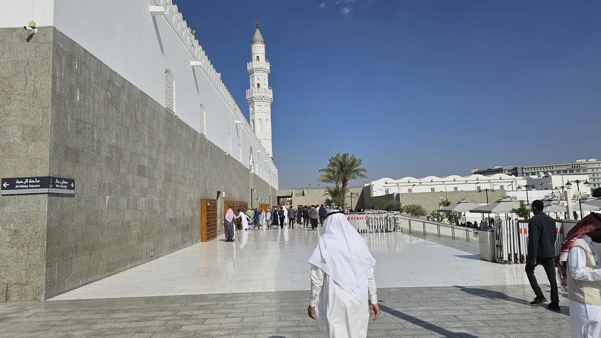 A visitor walking along the paved walkway beside Quba Mosque