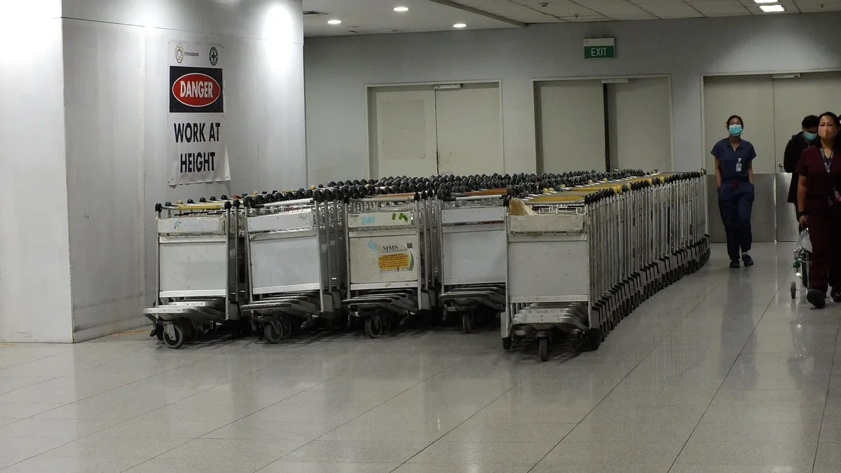 A row of stainless-steel luggage trolleys at an airport terminal